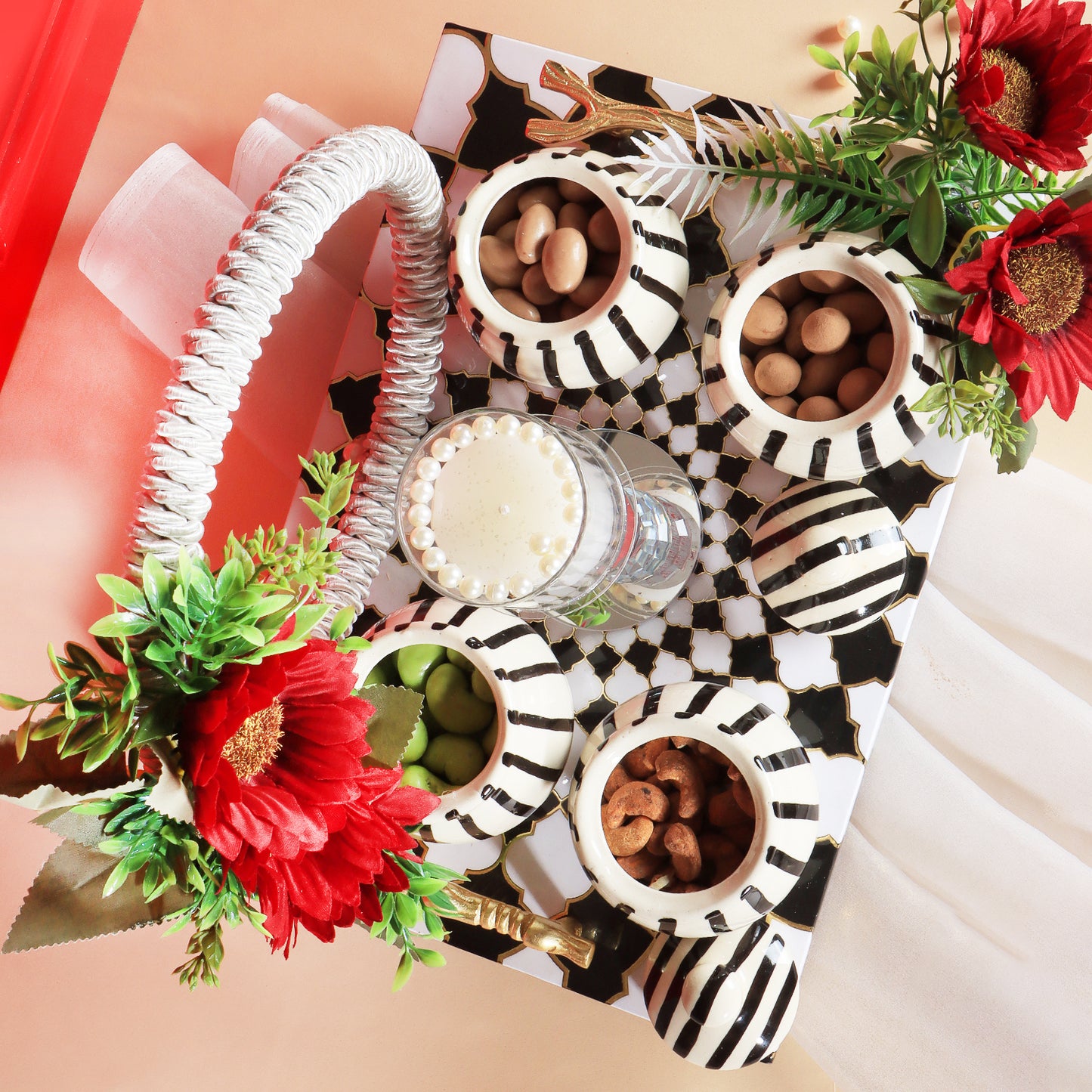 This gifting tray comes with 1 glass candle holder adorned with red flowers &amp; 4 ceramic abstract print jars filled with Oreo almonds , chocolate raisins, Pista flavored Cashew and Munchy masala cashew decorated in our MDF tray.